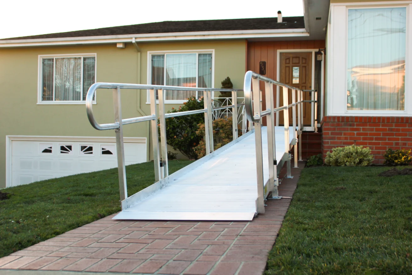 Aluminum wheelchair ramp installed at the front entrance of a house, leading from the sidewalk to the front door.
