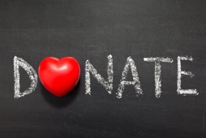 Chalkboard with the word "DONATE" written in white, where the letter "O" is replaced by a red heart-shaped object.