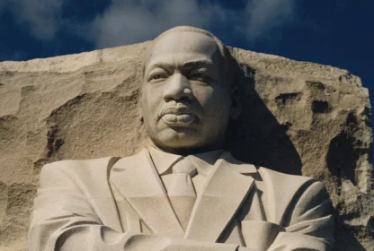 A stone statue of a man wearing a suit, part of a larger monument, set against a backdrop of a clear sky.