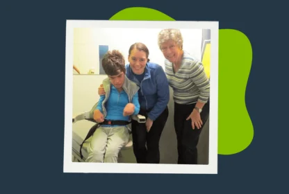A person in a medical lift is positioned next to two others who are smiling. The background includes a green shape on a dark backdrop.
