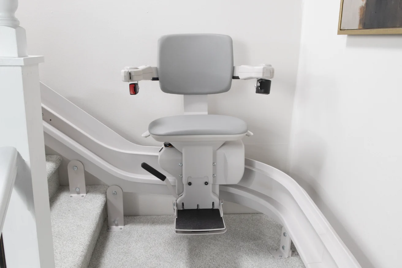 A gray stairlift is installed on a staircase with light-colored carpet, designed to assist individuals with mobility issues.