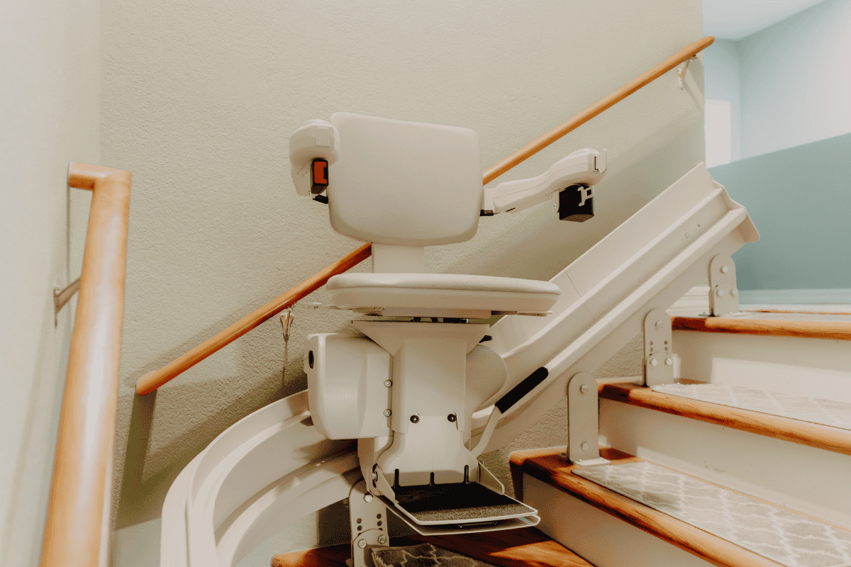 A stairlift is attached to a staircase with wooden steps and a railing, designed to assist with mobility on a curved area.