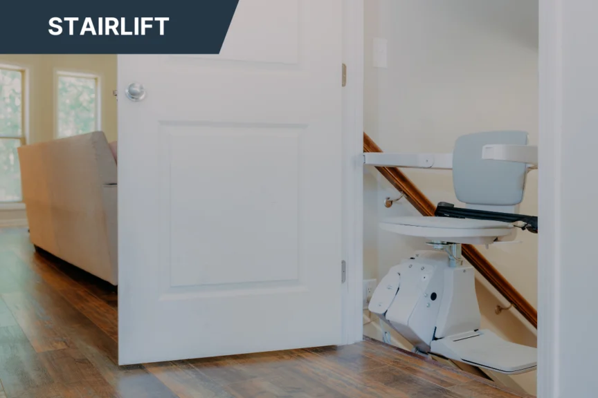 A stairlift is installed next to a wooden staircase in a home, with sunlight coming through the windows in the background.
