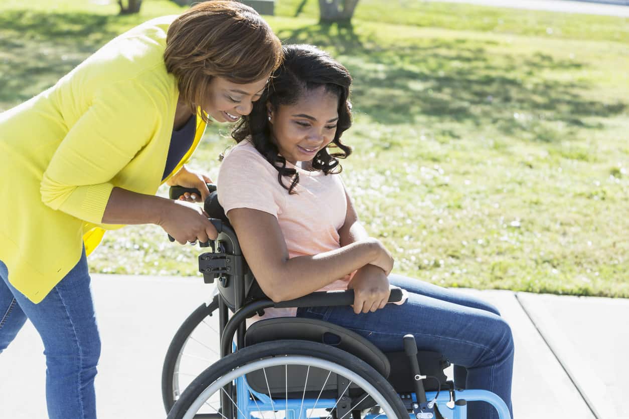 woman helps push a girl in a wheelchair down the sidewalk