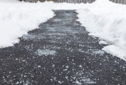 A snow-cleared path on the pavement is lightly covered with salt to prevent ice formation. Snow is piled on both sides of the path.