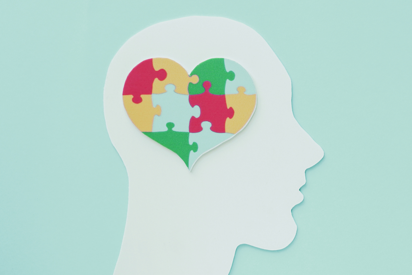 Silhouette of a head with a puzzle piece heart in multiple colors inside, symbolizing mental health or cognitive processes.