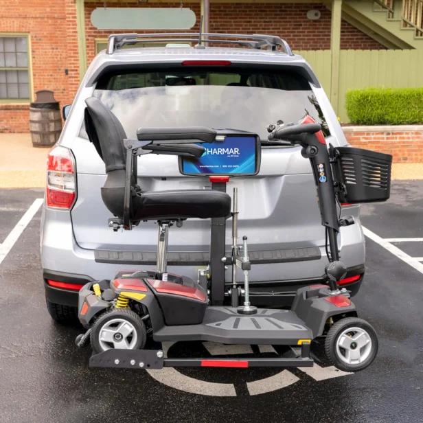 A mobility scooter is mounted on a lift attached to the back of a silver SUV parked in a lot.