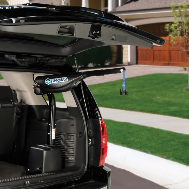 An SUV with the trunk open, showing a Harmar lift installed inside, designed to assist in lifting a power wheelchair or scooter. The vehicle is parked in a residential driveway.