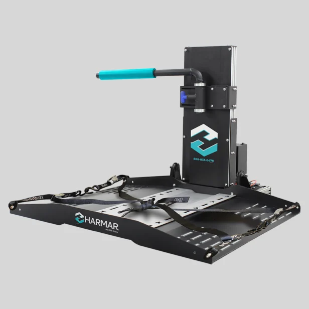 A black, motorized wheelchair lift with a blue handle and straps, branded with "Harmar" and contact information on the vertical section.