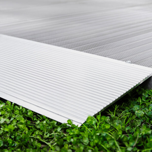 Close-up of a ribbed metal ramp on a green grass surface, showing the textured details of the ramp and the contrast with the grass.