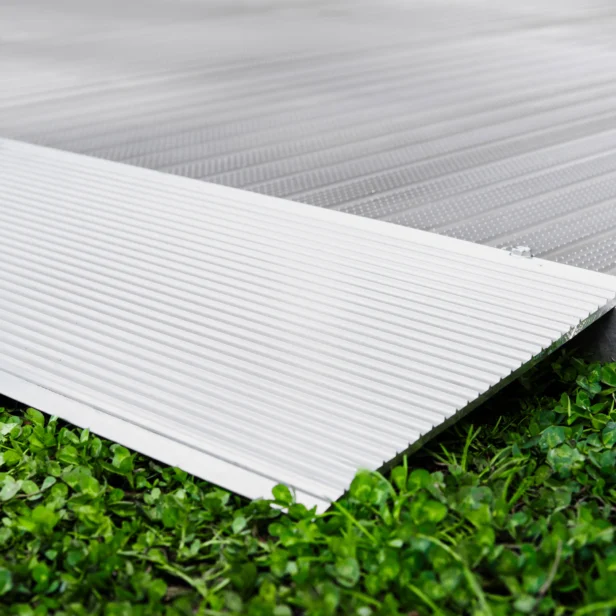 Close-up of a ribbed metal ramp on a green grass surface, showing the textured details of the ramp and the contrast with the grass.