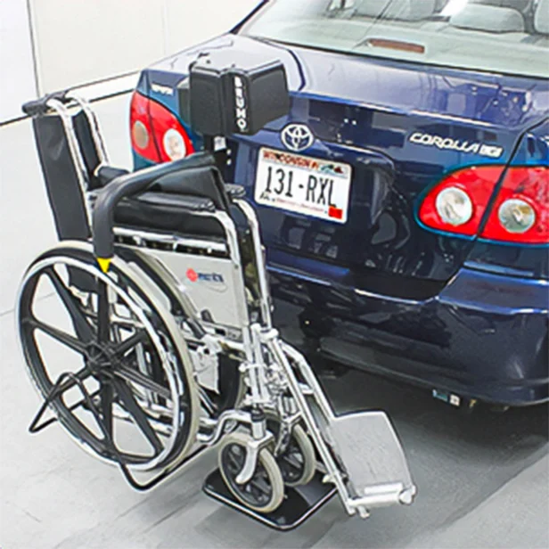 A black wheelchair is securely attached to the rear of a blue Toyota Corolla with a license plate reading "131-RXL".