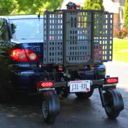 A black car with a Wisconsin license plate has a mobility scooter carrier attached to its rear, featuring a metal platform and signal lights.