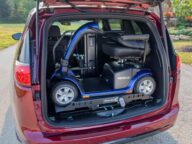 A mobility scooter is secured in the open trunk of a red car, ready for transportation.