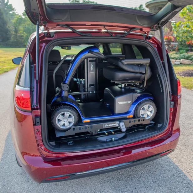 A mobility scooter is secured in the open trunk of a red car, ready for transportation.