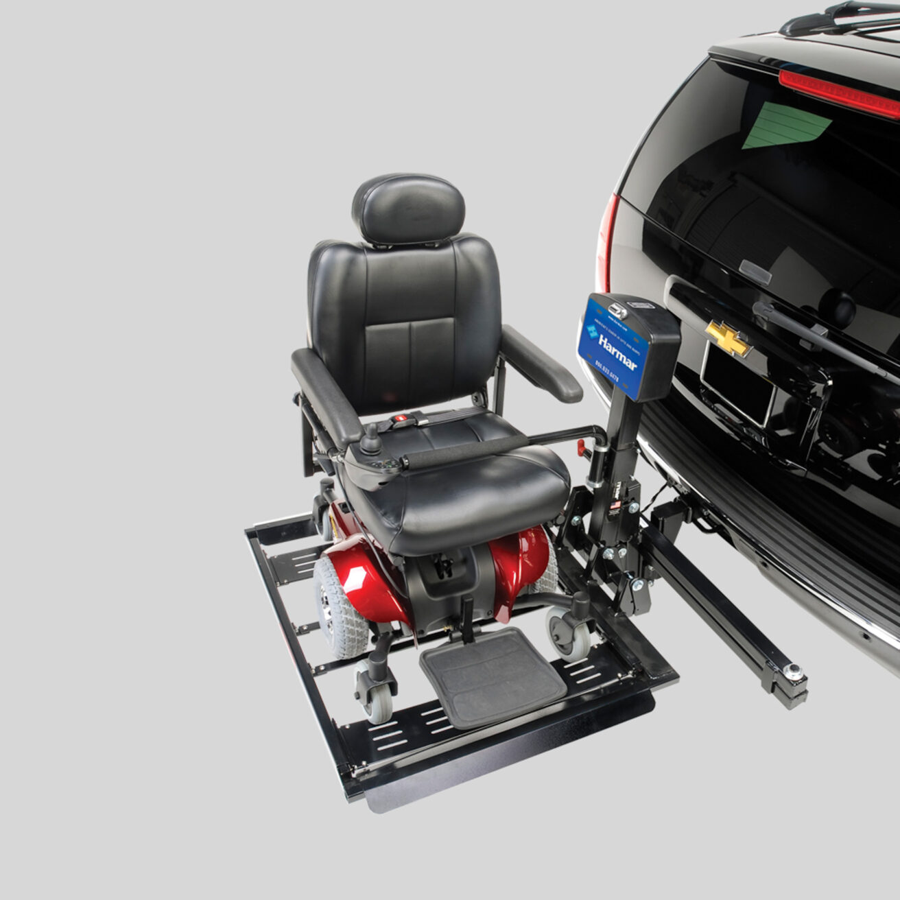 A black and red motorized wheelchair attached to a lift on the back of a black vehicle with a Chevrolet emblem.