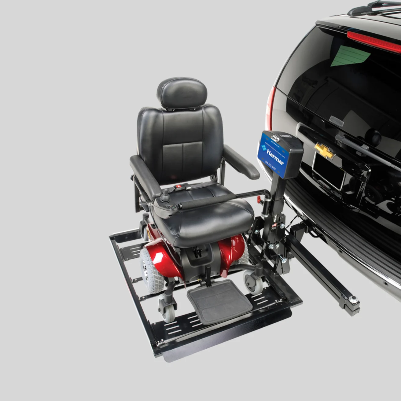 A black and red motorized wheelchair attached to a lift on the back of a black vehicle with a Chevrolet emblem.