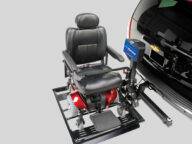 A black and red motorized wheelchair attached to a lift on the back of a black vehicle with a Chevrolet emblem.