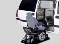 A white van with an open side door and an automated lift holding a motorized wheelchair, positioned for easy access.
