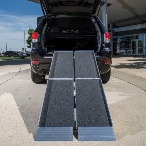 A black SUV with its rear hatch open and two portable aluminum ramps extending from the cargo area to the ground, positioned on a paved surface.
