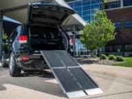 An open black SUV with a ramp extending from the trunk to the ground outside a modern building.