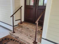 Front porch with brick steps leading to a wooden door, featuring handrails on both sides and a doormat with the word "hello.