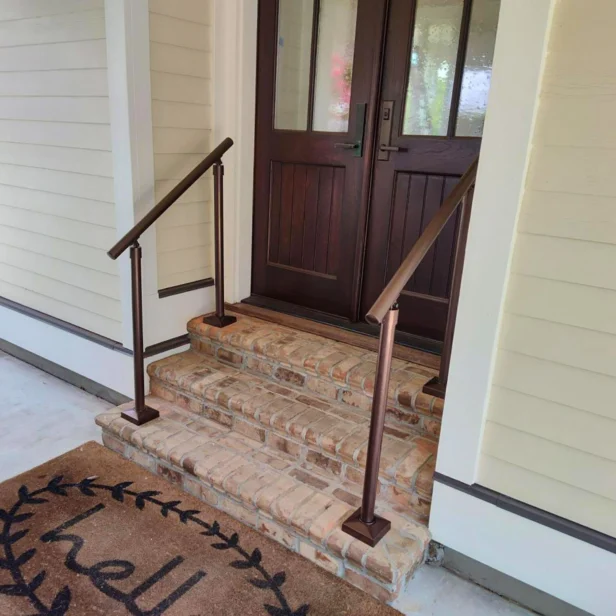 Front porch with brick steps leading to a wooden door, featuring handrails on both sides and a doormat with the word "hello.