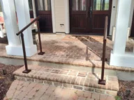 Front entryway of a house with wooden double doors, brick steps, and metal handrails on both sides leading up to a small porch.