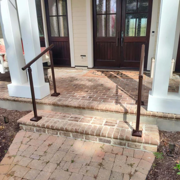 Front entryway of a house with wooden double doors, brick steps, and metal handrails on both sides leading up to a small porch.