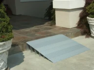 A metal access ramp set up at the edge of a tiled step, providing easier entry to a building.