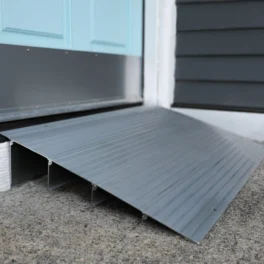 A gray metal wheelchair ramp is placed at the base of a doorway with a turquoise door and white door frame.