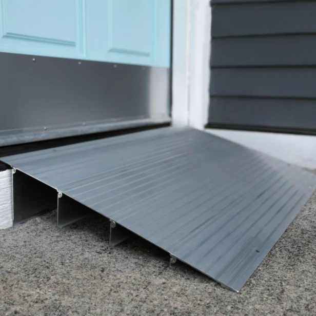 A gray metal wheelchair ramp is placed at the base of a doorway with a turquoise door and white door frame.