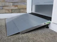 A silver wheelchair ramp is installed at the entrance of a building, providing accessibility over a concrete step.