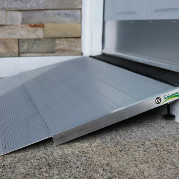 A silver wheelchair ramp is installed at the entrance of a building, providing accessibility over a concrete step.