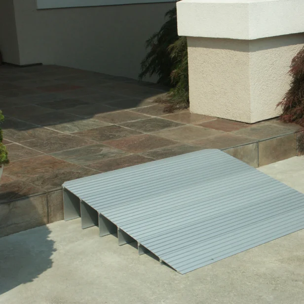 A metal access ramp set up at the edge of a tiled step, providing easier entry to a building.