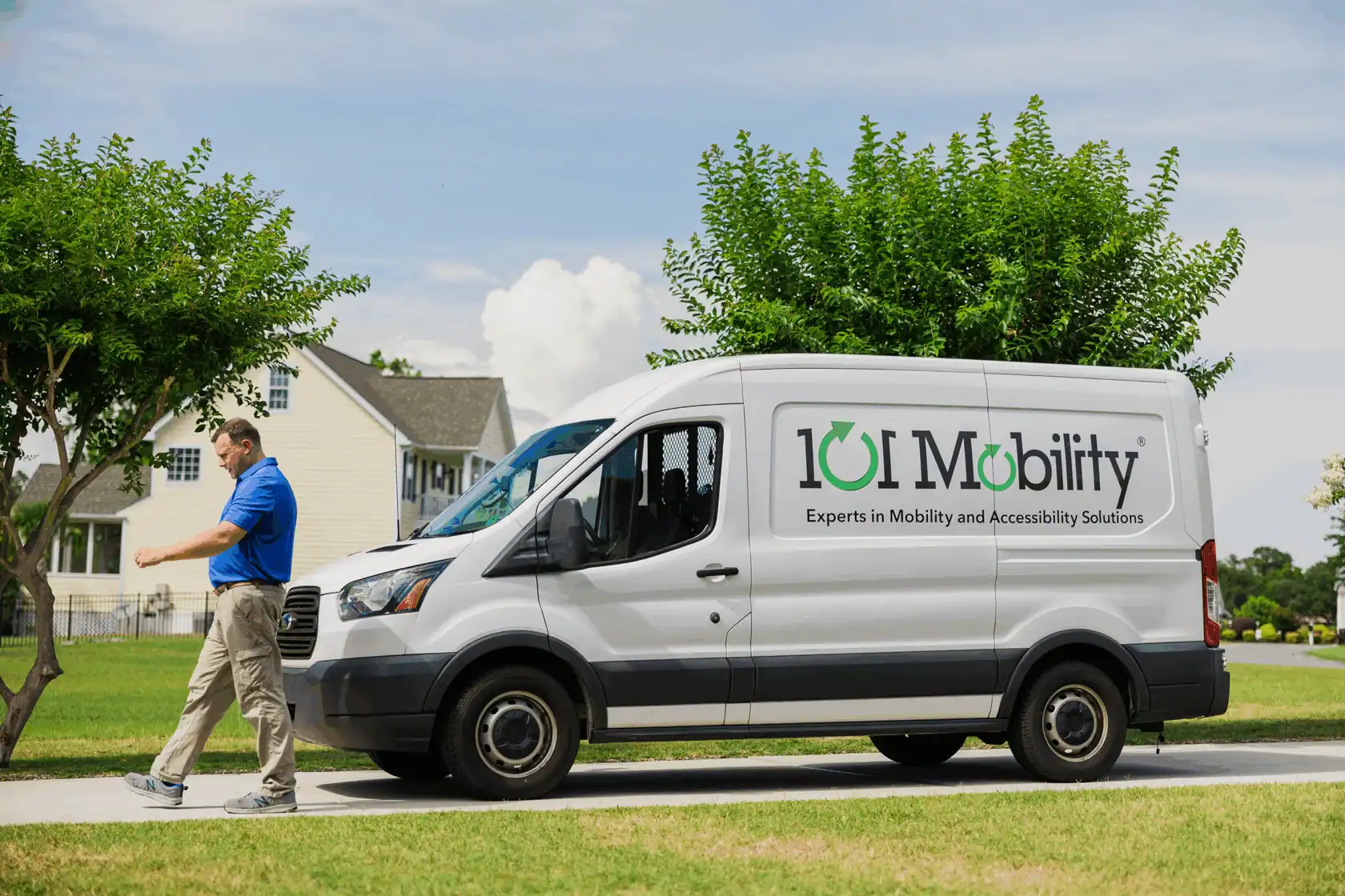 A man walks on a sidewalk next to a parked white van labeled "101 Mobility," featuring a logo and contact information for mobility and accessibility solutions.