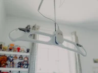 Overhead patient lift hangs from the ceiling by a cord in a room with shelves and a window in the background.
