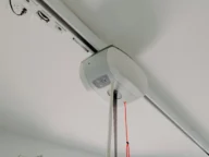 Close-up view of a overhead patient lift installed on the ceiling, with a red pull cord hanging down and a track extending across the ceiling.