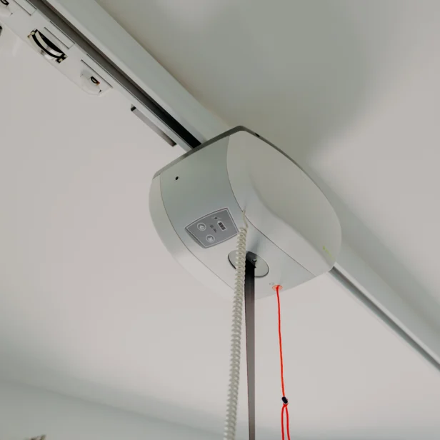 Close-up view of a overhead patient lift installed on the ceiling, with a red pull cord hanging down and a track extending across the ceiling.