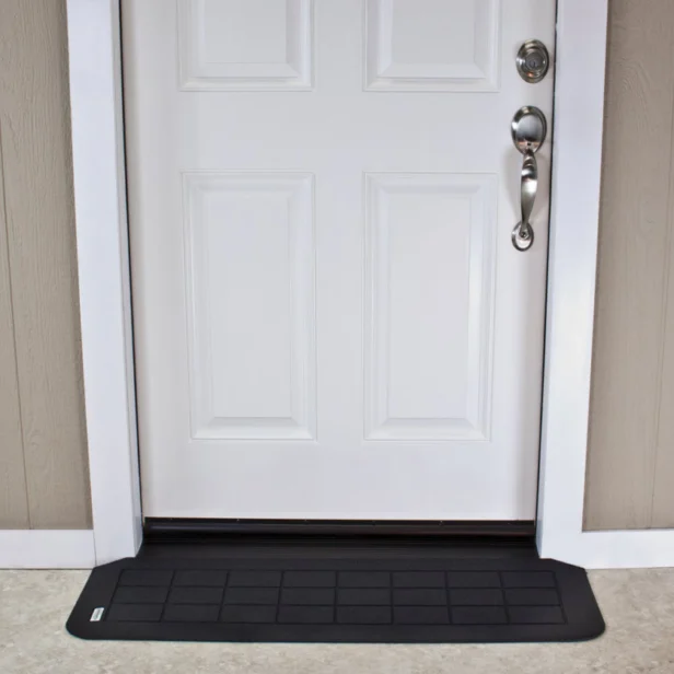 White door with a silver handle, surrounded by a light brown wall panel. A black rectangular mat lies centered in front of the door.
