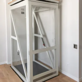 Glass residential elevator with metal frame installed indoors, featuring a control panel inside and the Savaria logo in the lower left corner.