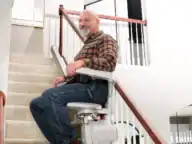 Smiling man riding a Bruno Elan SRE-5000 stairlift up a straight staircase