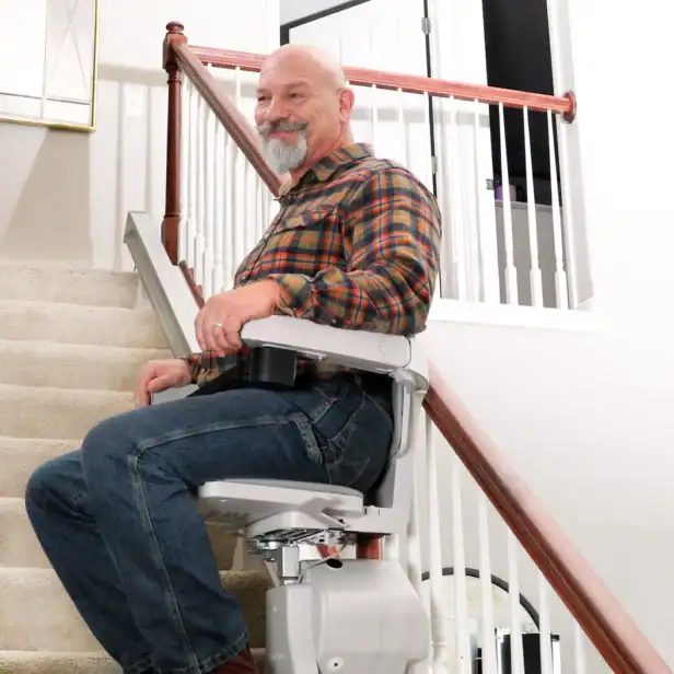 Smiling man riding a Bruno Elan SRE-5000 stairlift up a straight staircase