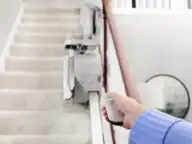 Hand pressing a wireless remote to call a folded Bruno Elan SRE-5000 stairlift