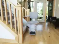 A stair lift chair is installed on a staircase in a bright, modern home with wood floors and large windows.