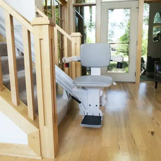 A stair lift chair is installed on a staircase in a bright, modern home with wood floors and large windows.