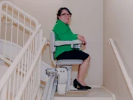 a woman smiling as she uses a bruno elite curved stairlift.