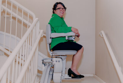 a woman smiling as she uses a bruno elite curved stairlift.