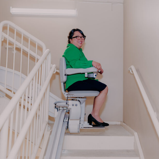 a woman smiling as she uses a bruno elite curved stairlift.