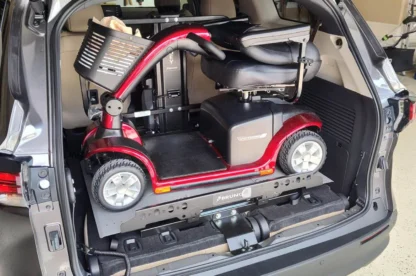 A red mobility scooter securely placed in the open trunk of a gray vehicle.